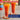 Two tall glasses of orange-colored syrup or juice on round coasters, with a blurred bottle in the background and promotional text overlays reading '33% More Flavor, For Less.' and 'More Syrup, More Savings Upgrade to 1 Liter Torani.